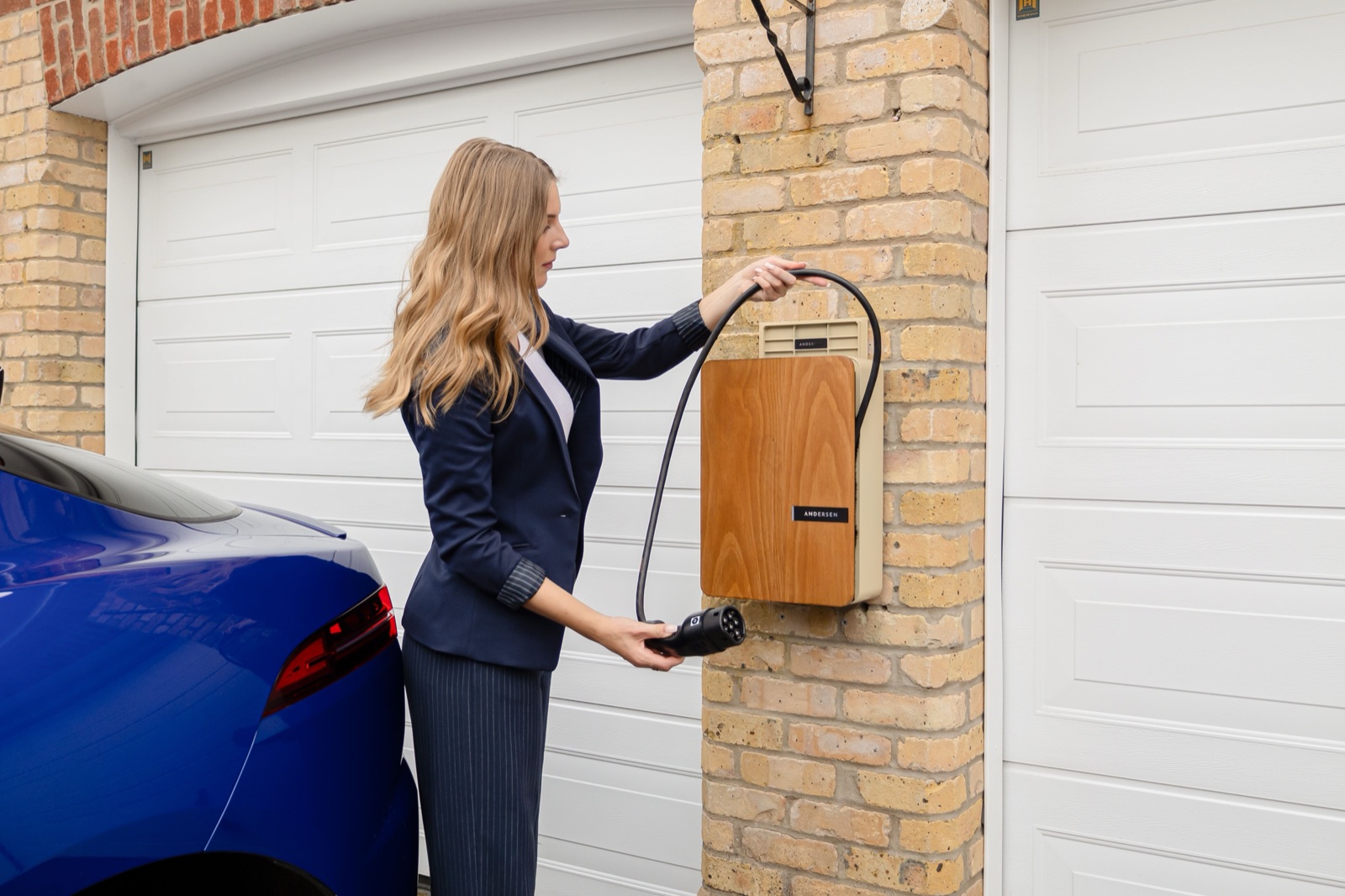 Elektroauto lädt an einer Wallbox an der Backsteinwand einer Garage